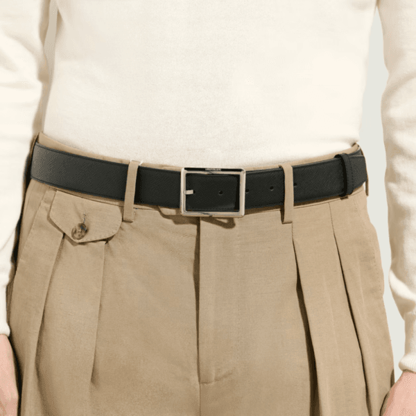 Cintura Montblanc Sartorial nera indossata su pantaloni beige con pieghe e tasca laterale, fibbia rettangolare lucida.
